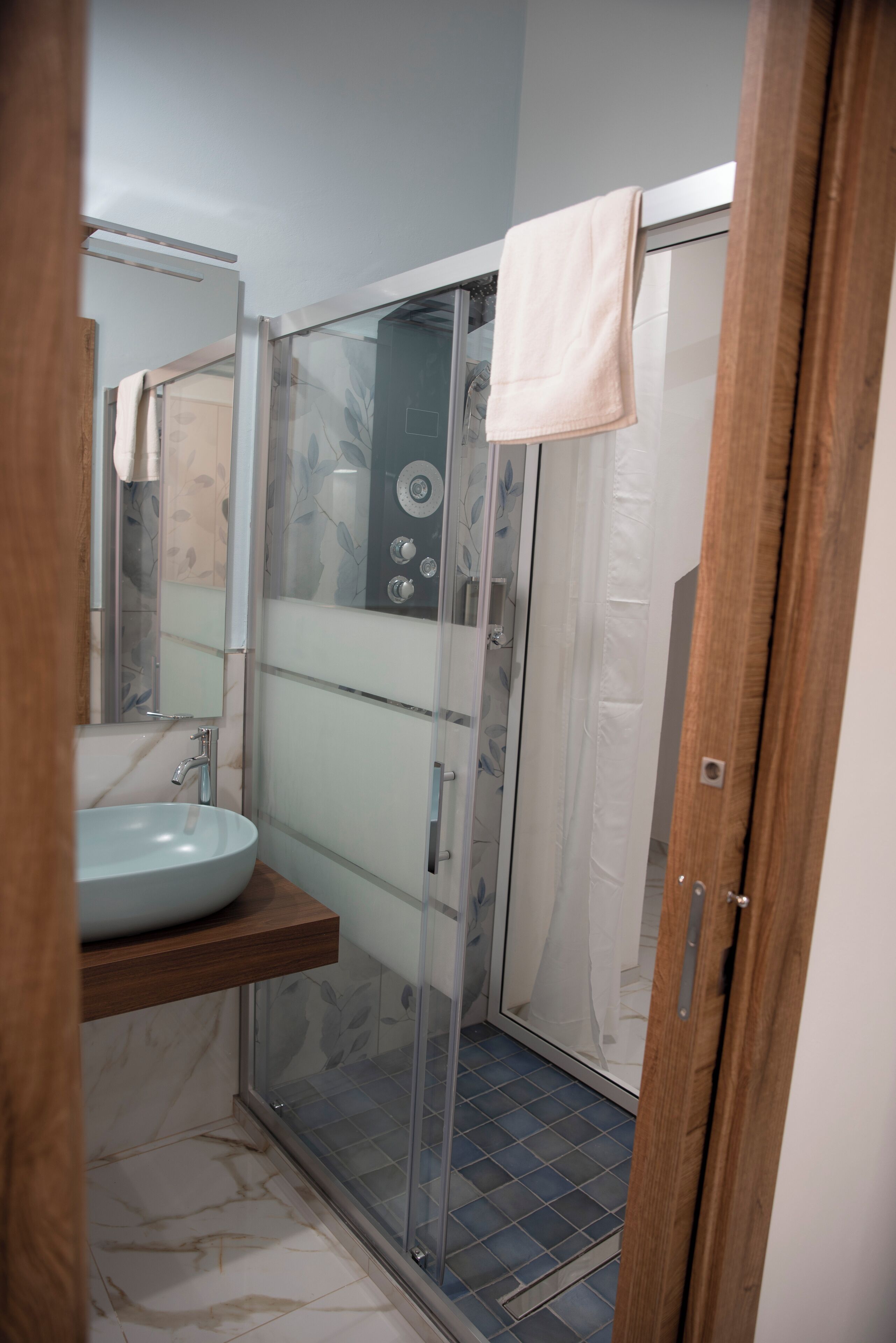 Ein Badezimmer mit einer gläsernen Duschkabine, einem Marmorboden und einem Holzausstattung mit Waschbecken.