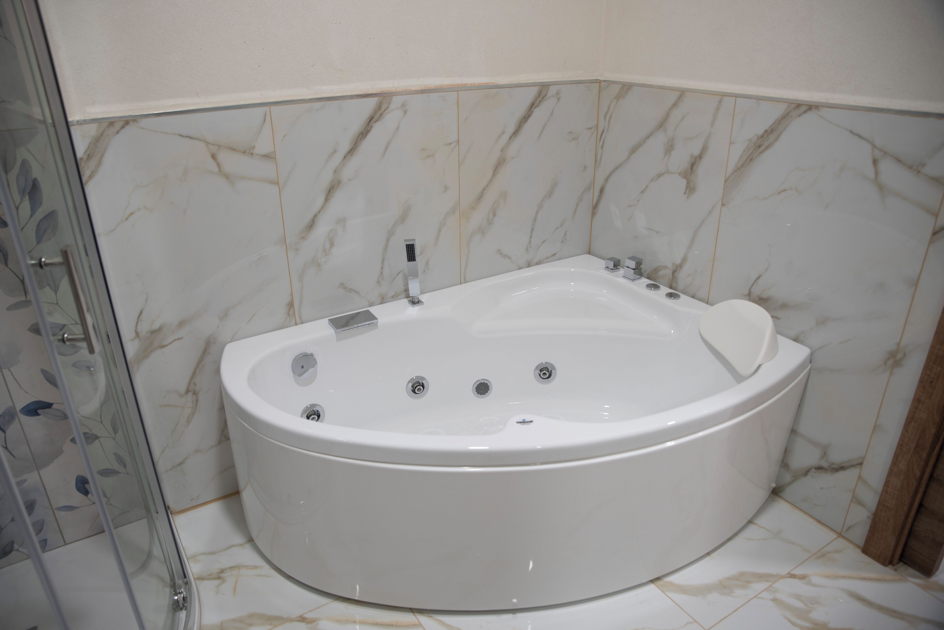 Een groot, wit, vrijstaand bad in een badkamer met marmeren wanden en een glazen douchecabine.