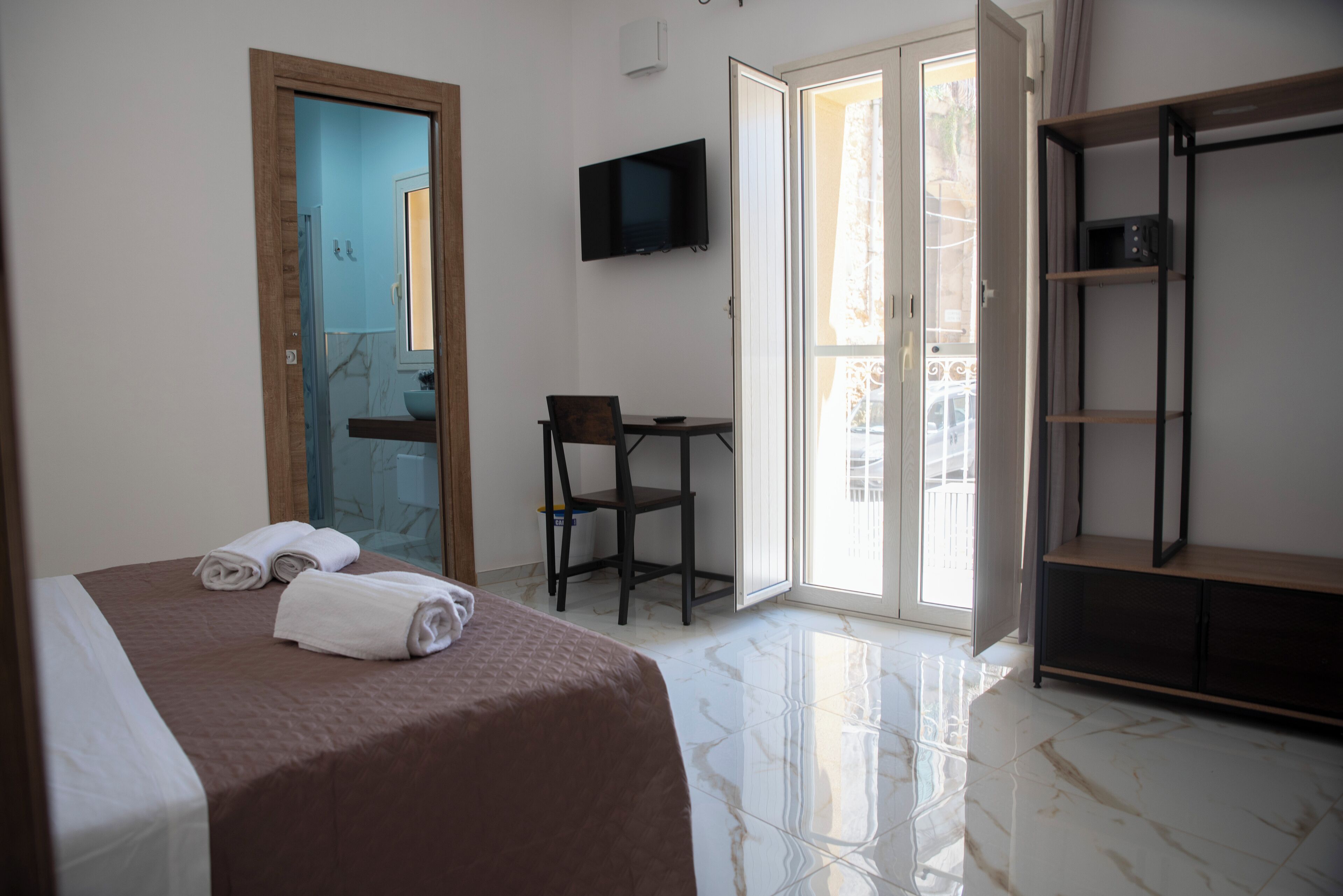 A hotel room with a bed, a desk, a chair, a TV, and a wardrobe.