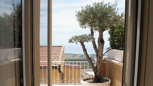 Un balcón con un árbol en maceta, suelo de baldosas y vistas al mar.