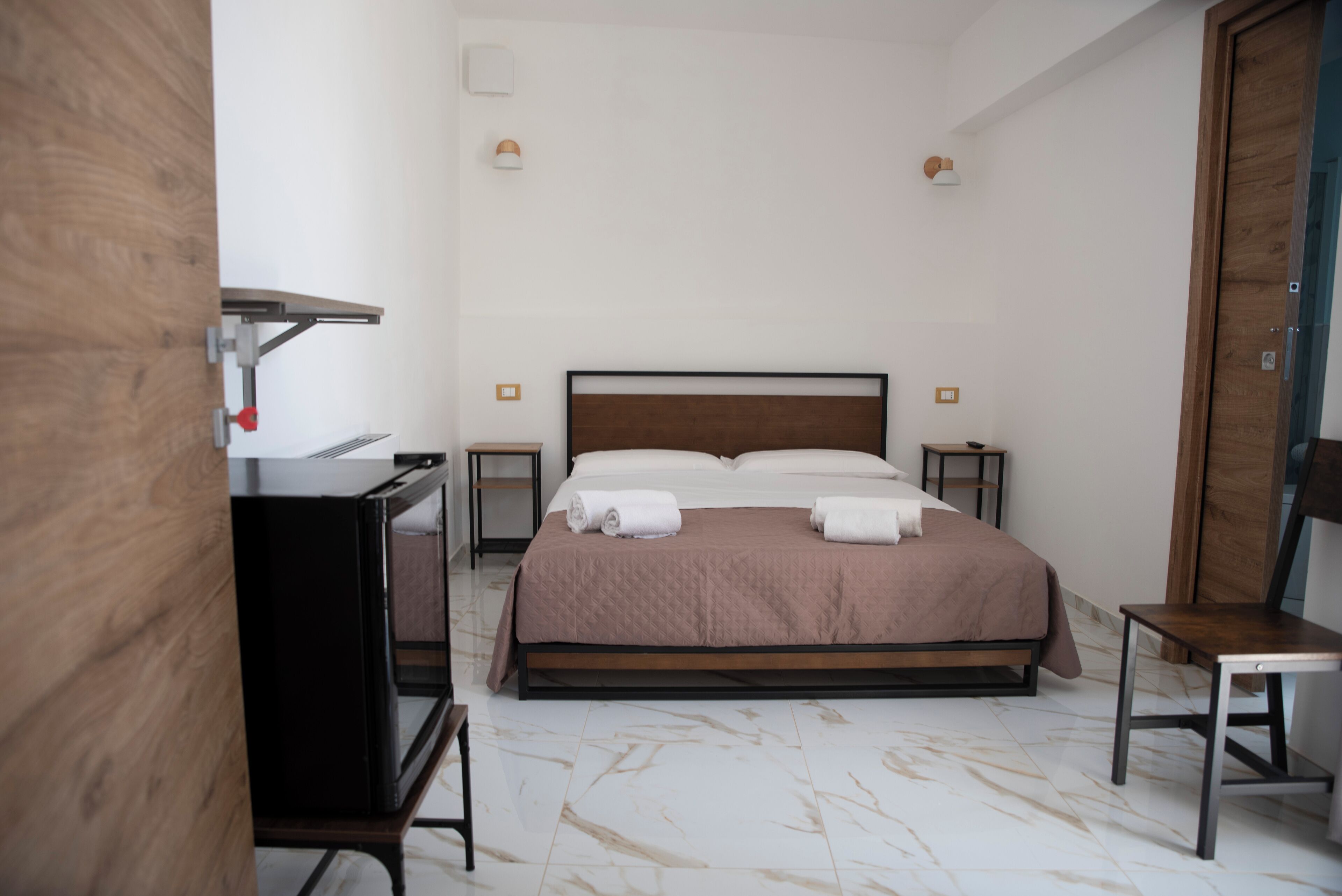 A neatly arranged bedroom with a bed, bedside tables, a desk, and a chair.