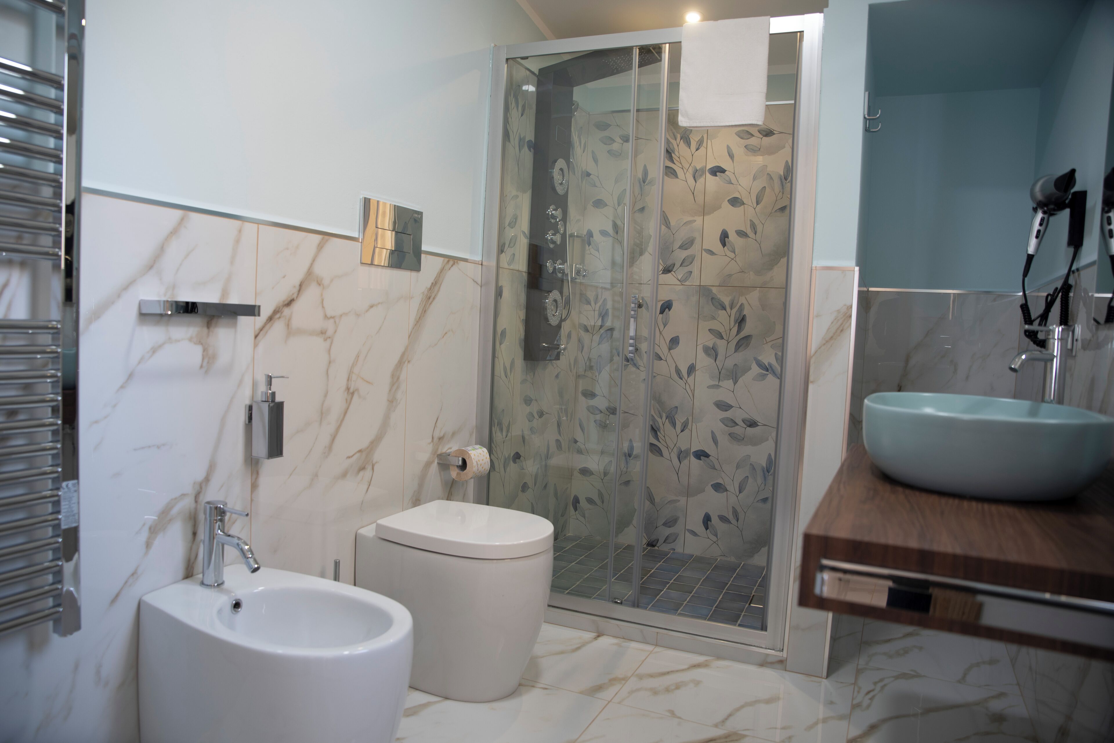 A modern bathroom with a marble floor, a white sink, a bidet, and a glass-enclosed shower.