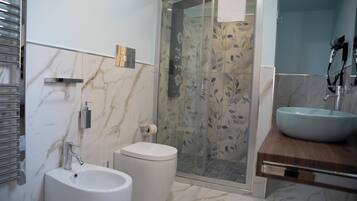 A modern bathroom with a marble floor, a white sink, a bidet, and a glass-enclosed shower.