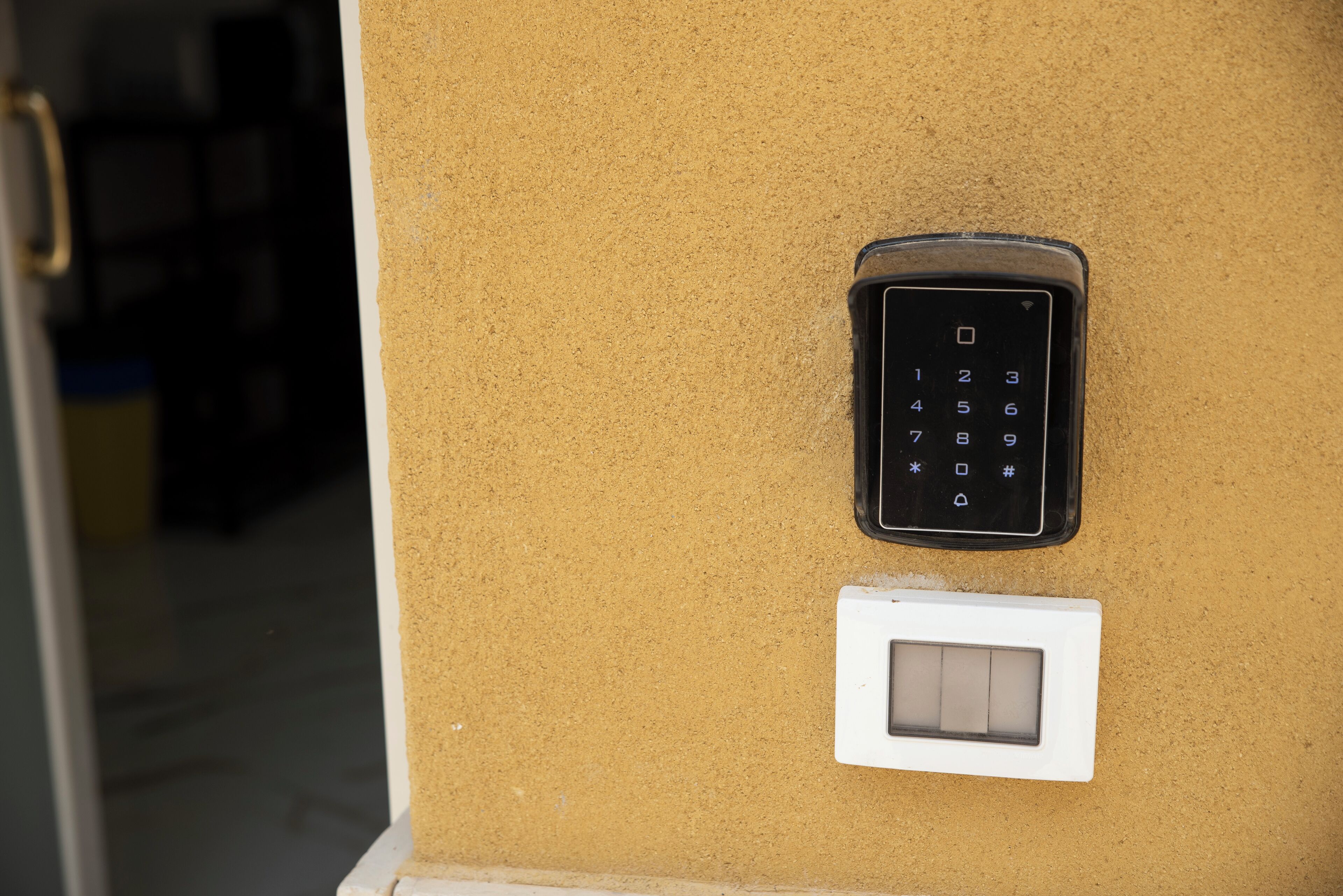 A keypad and a light switch mounted on a textured wall, likely part of a door mechanism.