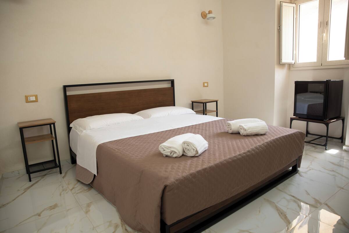 A hotel room with a large bed, two bedside tables, a television, and a window.