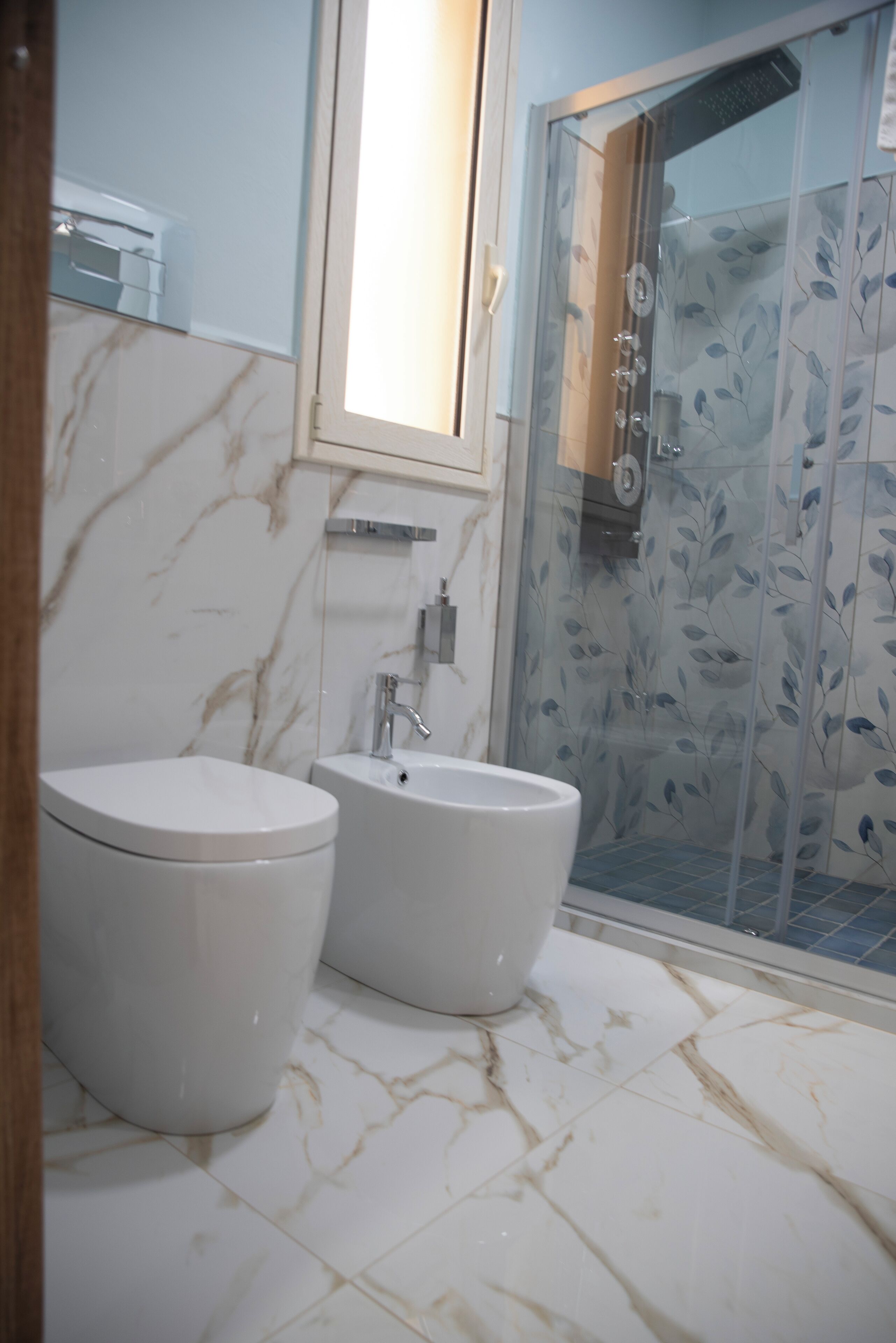 A bathroom with two toilets, a sink, and a glass-enclosed shower area.