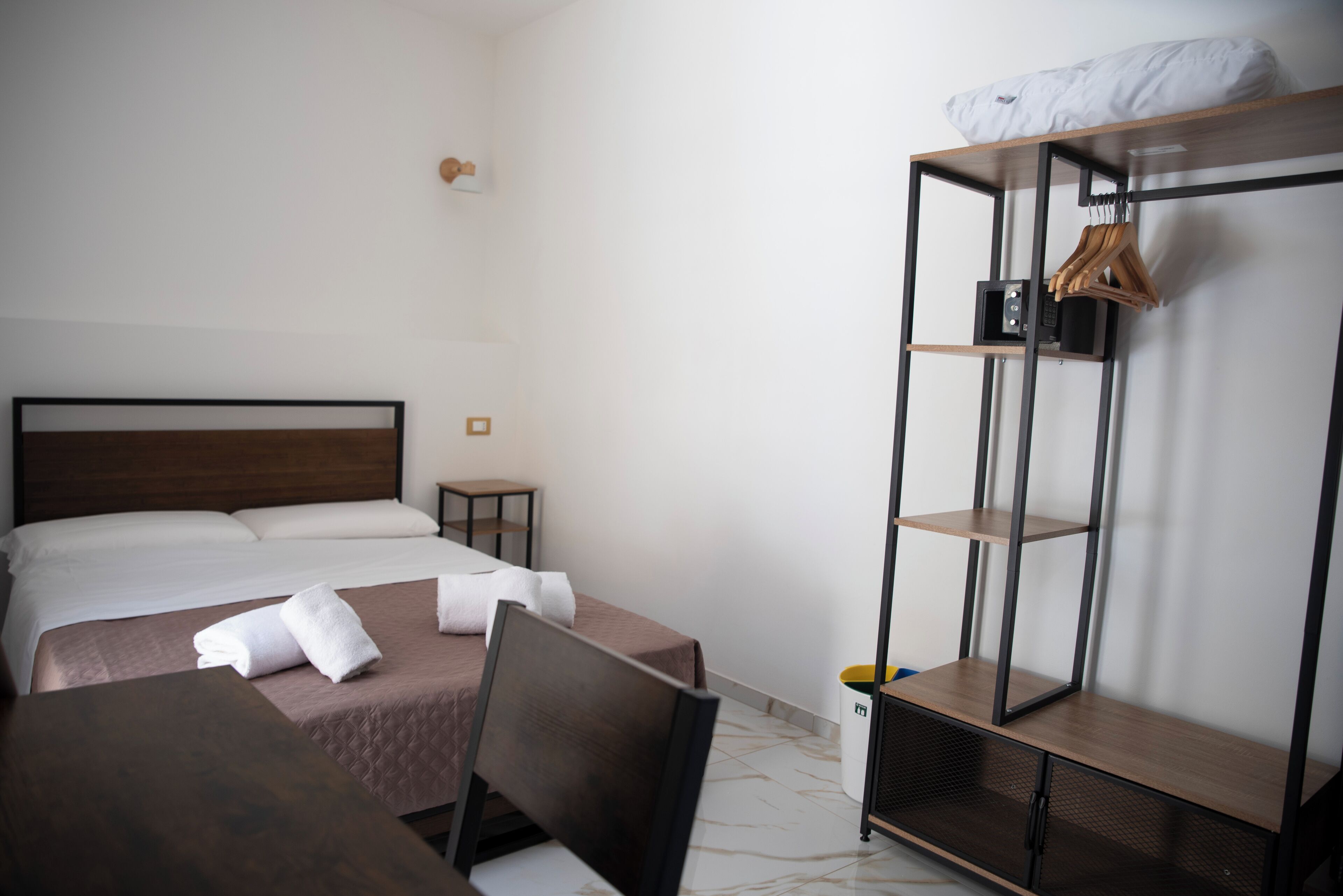 A hotel room with a bed, a desk, a chair, a wardrobe, and a small table.