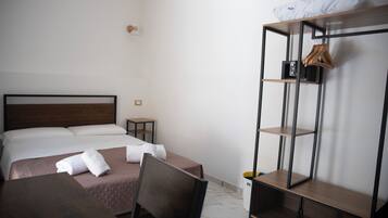 A hotel room with a bed, a desk, a chair, a wardrobe, and a small table.