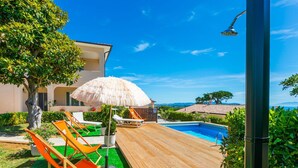 A wooden deck with a pool, lounge chairs, and a thatched umbrella.