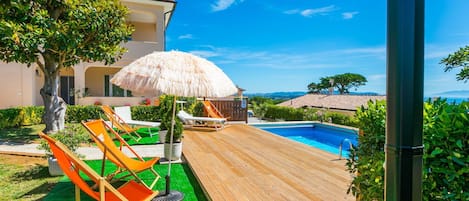 A wooden deck with a pool, lounge chairs, and a thatched umbrella.