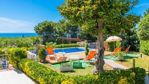 A pool area with lounge chairs, a pergola, and a view of the sea.