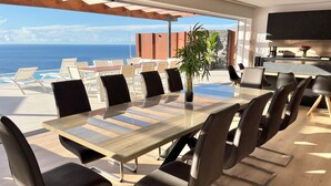 A modern dining area with a glass table and black chairs, overlooking a pool and the ocean.