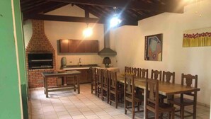 A spacious kitchen with a long dining table and chairs, a brick oven, and a tiled floor. - Charming place near SP (Caioçara Jarinu)