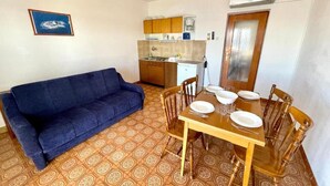 Un espace de vie compact comprenant un canapé, une table à manger, des chaises et un coin cuisine.