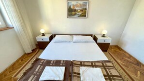 Un lit double avec une couette blanche, deux oreillers blancs et une couvre-lit marron à motifs. Il y a deux tables de chevet avec des lampes, un tableau représentant un paysage de montagne accroché au mur et un plancher en bois.