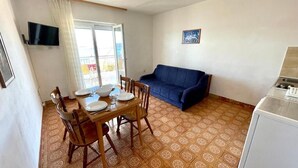 Un coin repas avec une table dressée pour quatre personnes, un canapé bleu et un téléviseur fixé au mur.