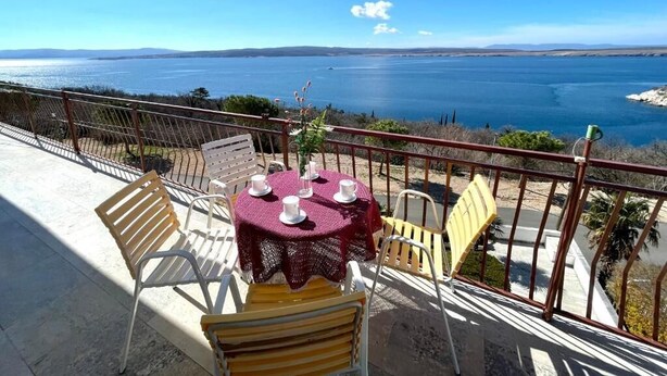 Une terrasse avec une table dressée pour deux personnes, offrant une vue sur une vaste étendue d’eau et sur la terre ferme au loin.