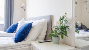 A neatly made bed with white and blue pillows, a bedside table with a remote control and a potted plant, and a large mirror reflecting the room. - Stunning private villa for 6 people with WIFI and TV (Isle Of Skye)