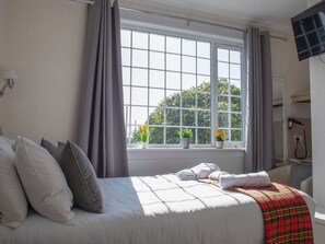 Una habitación de hotel con un ventanal grande, una cama con almohadas, una manta escocesa roja y un secador de pelo en un estante.