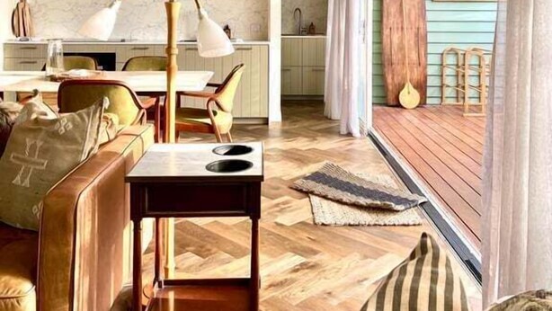 Amplia sala de estar con suelo de madera en espiga, un sofá, una mesa de centro y un comedor con mesa y sillas.