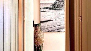 Un pasillo con piso de madera, un cuadro grande con una escena de playa y un jarrón decorativo.
