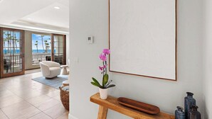 Un soggiorno moderno con una grande finestra vista spiaggia, un divano bianco, un tavolino consolle in legno con oggetti decorativi e un'opera d'arte incorniciata appesa al muro.