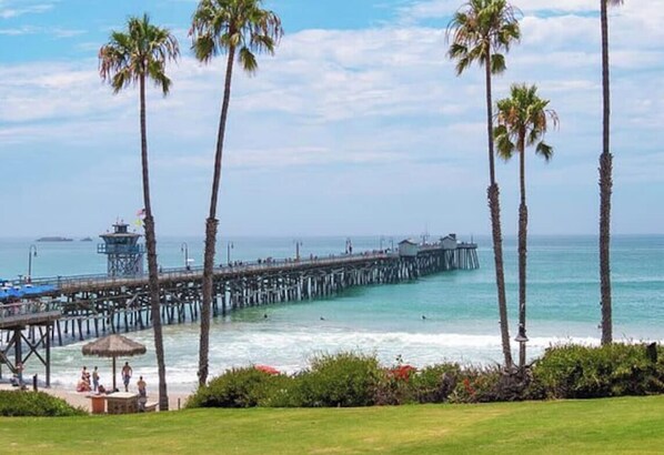 A pier extending into the ocean with palm trees and a grassy area in the foreground. - Lux Oceanview Retreat with Bikes and Walk to Beach (San Clemente)