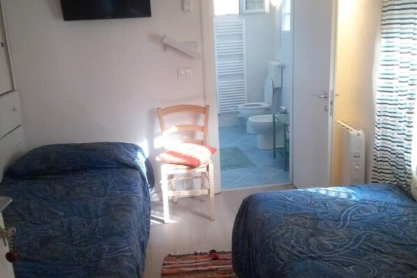A room with two beds, a chair, a small table, and a view of the bathroom.