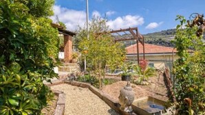 A garden with a pergola, a water feature, and a brick building in the background.