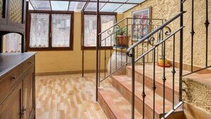 A room with a wooden cabinet, a staircase with a metal railing, and a view through a window with curtains.