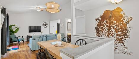 Ein modernes Wohnzimmer mit einem Holzesstisch, einem hellblauen Sofa und einem großen Wandbild.