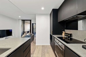 A modern kitchen with a central island, a built-in oven, and a dining area with a sofa. - Stylish Apartment in Canberra CBD (Reid)