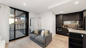 A modern apartment with a grey sofa, a kitchen with dark cabinets, and a sliding glass door leading to an outdoor area.