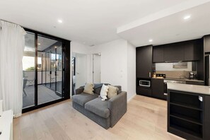 A modern apartment with a grey sofa, a kitchen with dark cabinets, and a sliding glass door leading to an outdoor area. - Stylish Apartment in Canberra CBD (Reid)