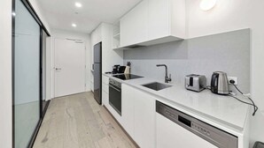 Une cuisine moderne avec des meubles blancs, un four encastré, un lave-vaisselle et un évier avec un robinet.