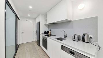 A modern kitchen with white cabinets, a built-in oven, a dishwasher, and a sink with a faucet.