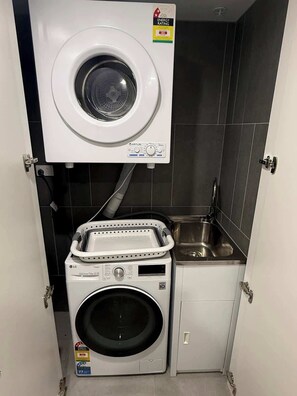 Ein kleiner Waschraum mit einer Waschmaschine mit Frontlader, einem Trockner mit Oberlader und einem kleinen Spülbecken.