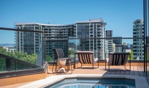 A rooftop terrace with a pool, two chairs, and a table.
