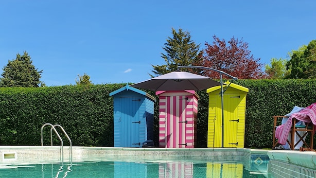 A swimming pool with three colorful sheds in the background.