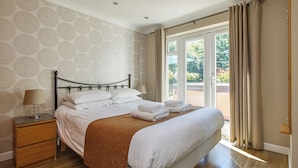 A neatly made bed with white linens and a brown throw, a bedside table with a lamp, and a patterned wallpaper.