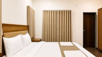 A hotel room with a bed, a bedside telephone, a wooden headboard, a window with curtains, and a door.