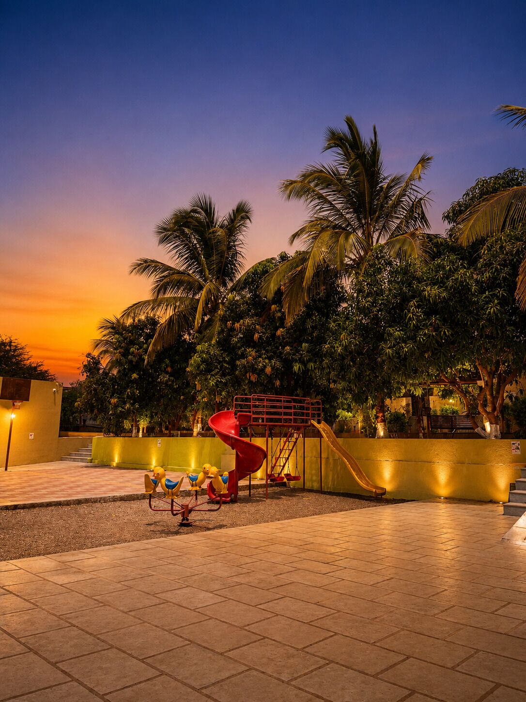 Un parque infantil con toboganes y columpios, rodeado de palmeras y un cielo al atardecer.