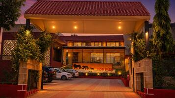 A hotel with a red-tiled roof, a central entrance with a lion statue, and a paved driveway.