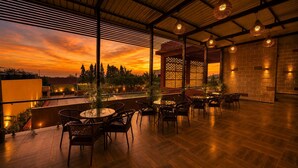 Une terrasse extérieure dotée d’un plancher en bois, de chaises et de tables en osier, offrant une vue imprenable sur le coucher de soleil.