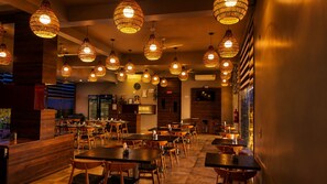 Een restaurantinterieur met meerdere tafels en hangende rieten lampen.