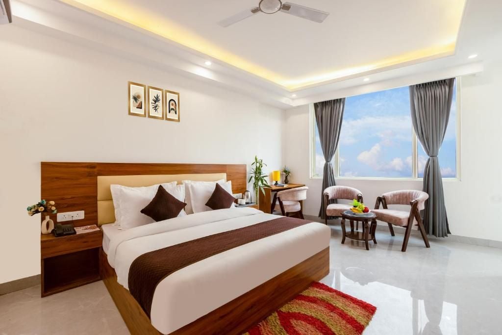 A hotel room with a large bed, a desk, two chairs, a ceiling fan, and a window with curtains.