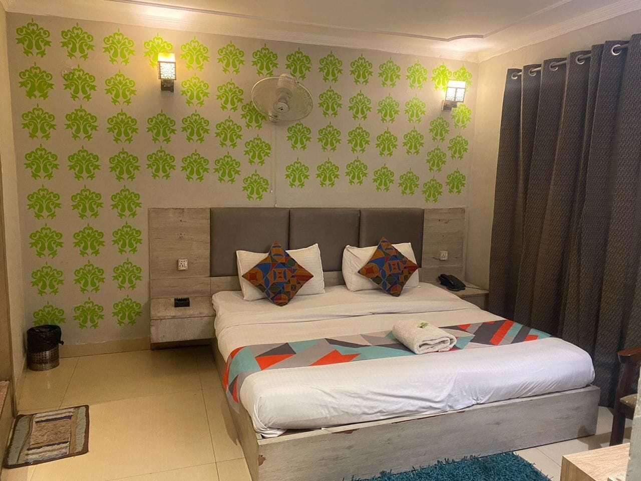 Un dormitorio con una cama, dos luces en la pared, un ventilador de techo y un papel tapiz estampado.