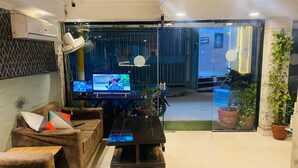 A living area with a sofa set, a coffee table, and a television. There is a potted plant and a motorcycle outside the window. - Hotel Metro Tower (New Delhi)