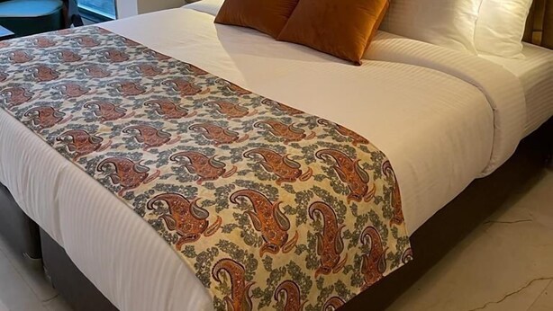 A hotel room with a large bed, a patterned bedspread, and a view of the outside through a window. - Hotel Metro Tower (New Delhi)