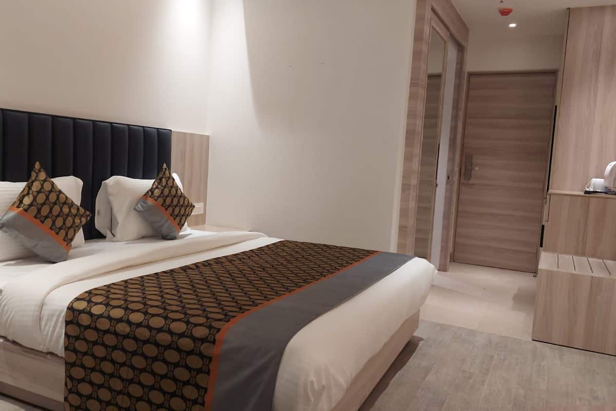 A modern hotel room with a large bed, a nightstand, a wardrobe, and a bathroom door.